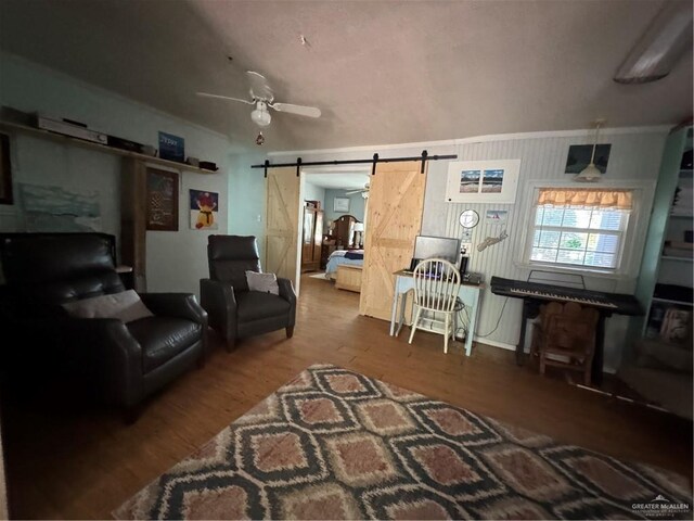 living room with ceiling fan, a barn door, wood-type flooring, and ornamental molding