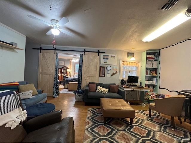 living room with a textured ceiling, a barn door, hardwood / wood-style flooring, and ceiling fan