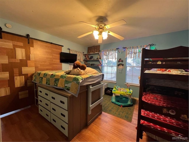 bedroom featuring a barn door, ceiling fan, and hardwood / wood-style flooring