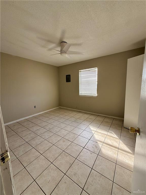 empty room featuring a ceiling fan, light tile patterned flooring, a textured ceiling, and baseboards