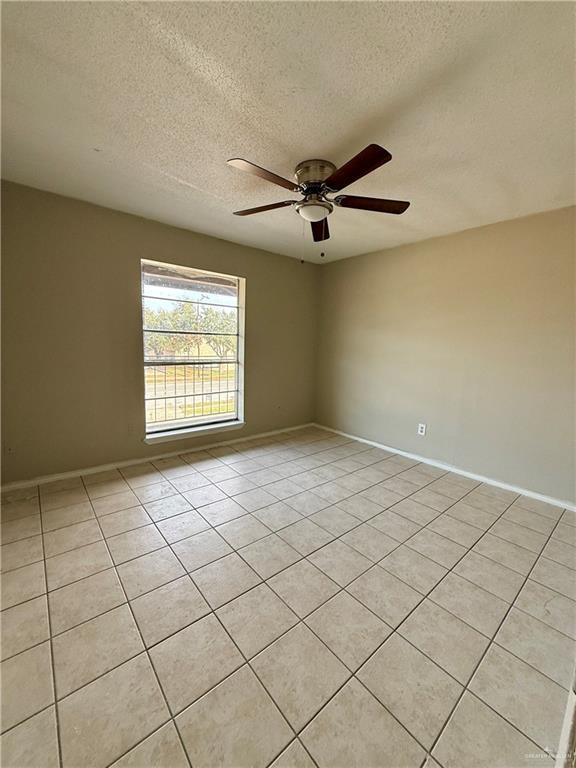 unfurnished room featuring light tile patterned floors, a textured ceiling, baseboards, and a ceiling fan