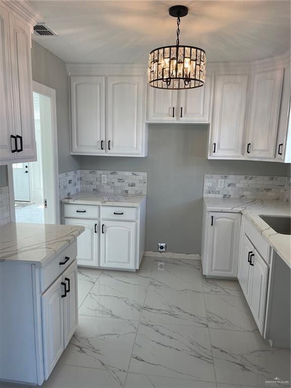 kitchen featuring backsplash, light stone counters, pendant lighting, a chandelier, and white cabinetry