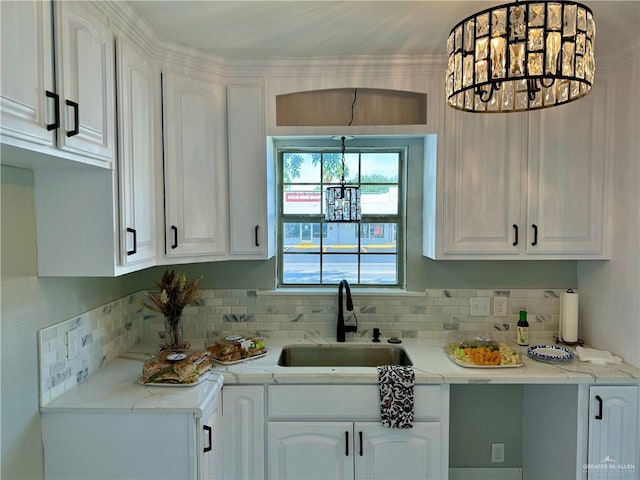 kitchen with tasteful backsplash, sink, an inviting chandelier, white cabinetry, and hanging light fixtures