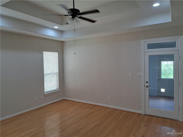 spare room featuring a tray ceiling, a wealth of natural light, ceiling fan, and light wood-type flooring