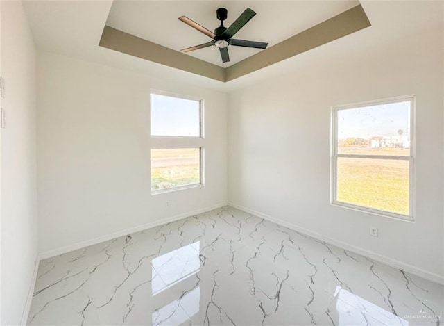 empty room with ceiling fan and a tray ceiling