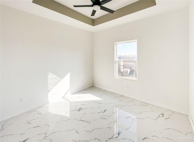 empty room with ceiling fan and a tray ceiling