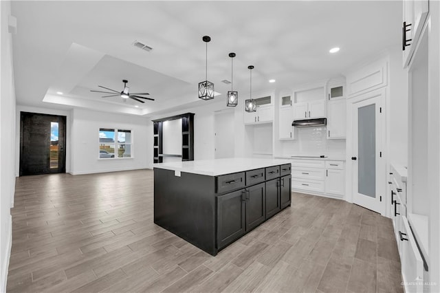 kitchen featuring white cabinetry, a center island, a raised ceiling, decorative light fixtures, and light wood-type flooring