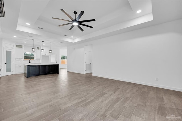 unfurnished living room with light hardwood / wood-style floors, a raised ceiling, ceiling fan, and sink