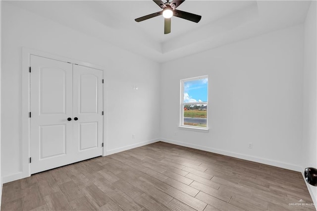 unfurnished bedroom featuring light wood-type flooring, a closet, a raised ceiling, and ceiling fan