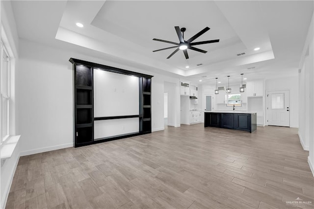 unfurnished living room with a tray ceiling, ceiling fan, light hardwood / wood-style floors, and sink