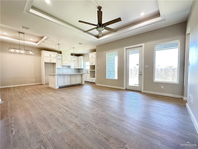 unfurnished living room featuring a raised ceiling, ceiling fan, and light hardwood / wood-style floors