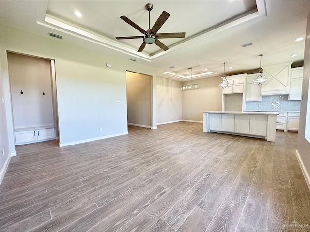 unfurnished living room with a raised ceiling, light hardwood / wood-style flooring, and ceiling fan with notable chandelier