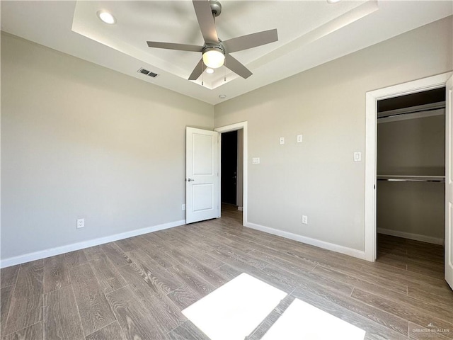 unfurnished bedroom with a tray ceiling, a closet, ceiling fan, and light hardwood / wood-style flooring