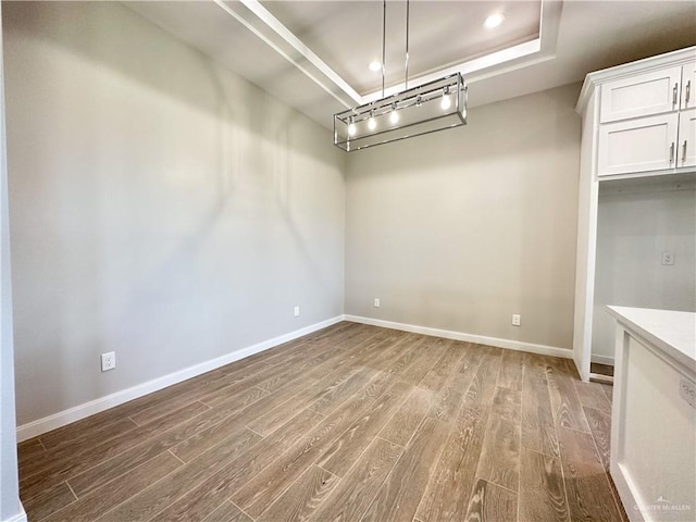 unfurnished dining area featuring a tray ceiling and wood-type flooring