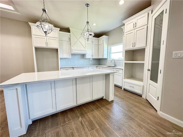 kitchen featuring dark wood-type flooring, sink, pendant lighting, white cabinets, and a center island