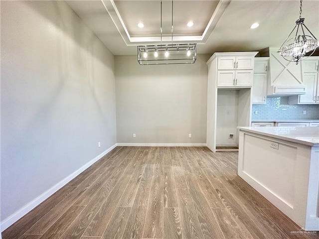 kitchen featuring light wood-type flooring, backsplash, a raised ceiling, decorative light fixtures, and white cabinetry