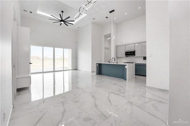 kitchen with ceiling fan, hanging light fixtures, a raised ceiling, a towering ceiling, and a kitchen island with sink