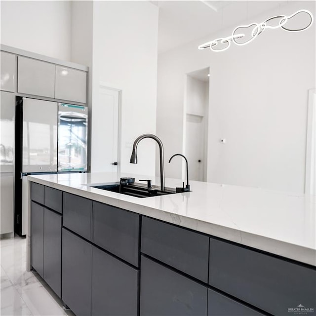 kitchen with light stone countertops, stainless steel refrigerator, gray cabinetry, and sink