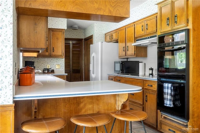 kitchen featuring kitchen peninsula, light tile patterned floors, a breakfast bar area, and black appliances