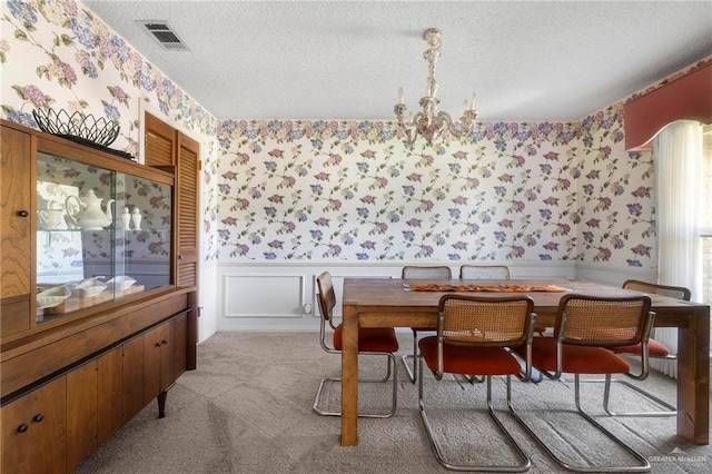 carpeted dining area with a chandelier and a textured ceiling