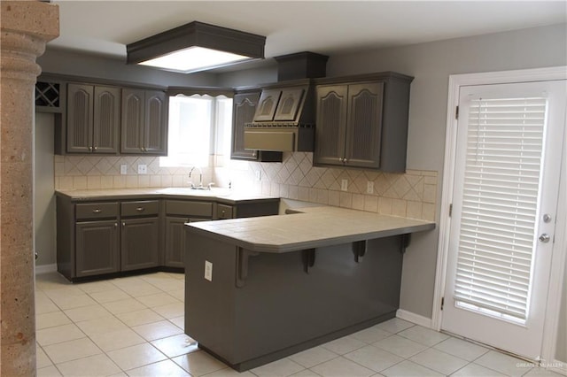 kitchen featuring a sink, light tile patterned floors, a peninsula, a kitchen bar, and tasteful backsplash