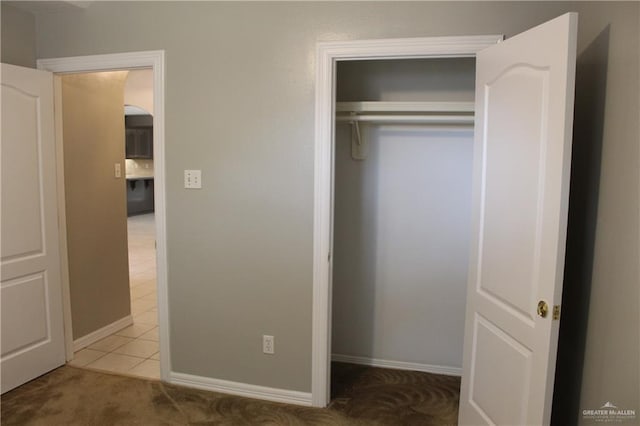 unfurnished bedroom featuring tile patterned flooring, a closet, carpet flooring, and baseboards