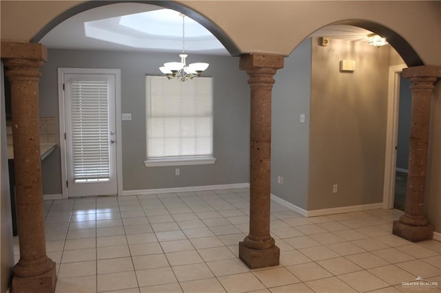 unfurnished dining area with light tile patterned flooring, a chandelier, arched walkways, a tray ceiling, and ornate columns