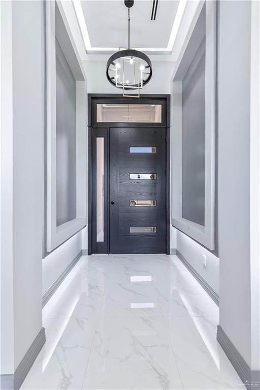 entrance foyer with a notable chandelier, a tray ceiling, and marble finish floor