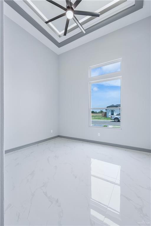 spare room with ceiling fan, a tray ceiling, marble finish floor, and baseboards