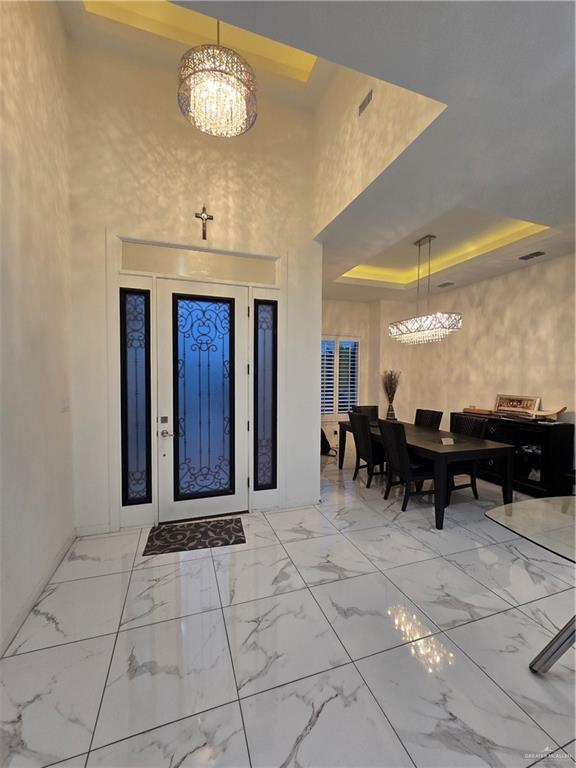 entryway featuring a raised ceiling, a towering ceiling, and an inviting chandelier