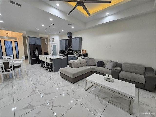 living room with ceiling fan, a tray ceiling, and sink