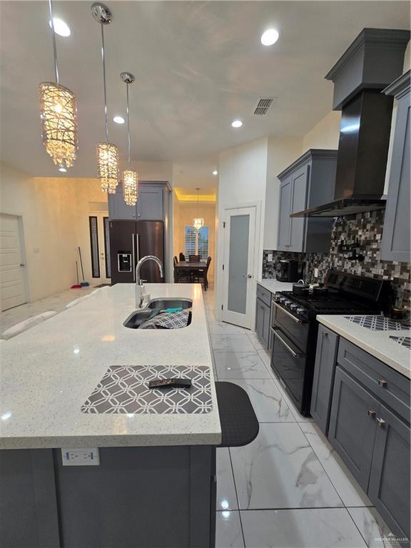 kitchen featuring decorative backsplash, black appliances, wall chimney range hood, pendant lighting, and sink