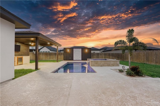 pool at dusk featuring an in ground hot tub and a patio area