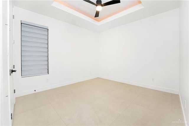 spare room with a tray ceiling, ceiling fan, and light tile patterned floors