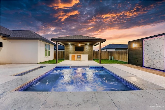 pool at dusk with exterior bar, an outdoor kitchen, and a patio area