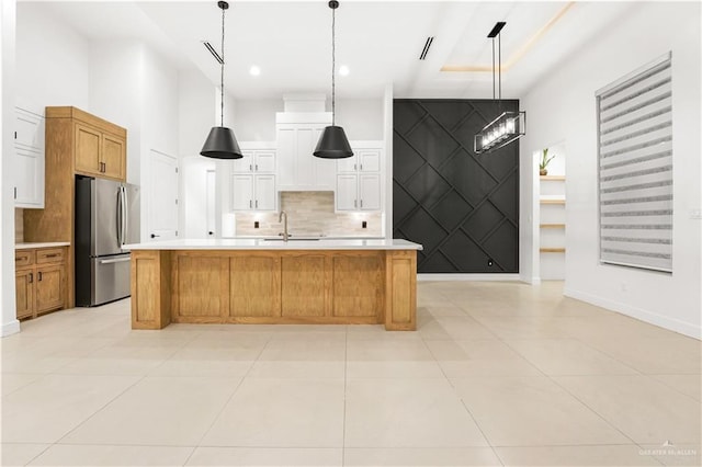 kitchen featuring sink, pendant lighting, a center island with sink, white cabinetry, and stainless steel refrigerator