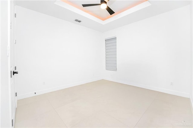 empty room featuring ceiling fan, a raised ceiling, and light tile patterned floors