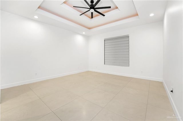 tiled spare room featuring a raised ceiling and ceiling fan