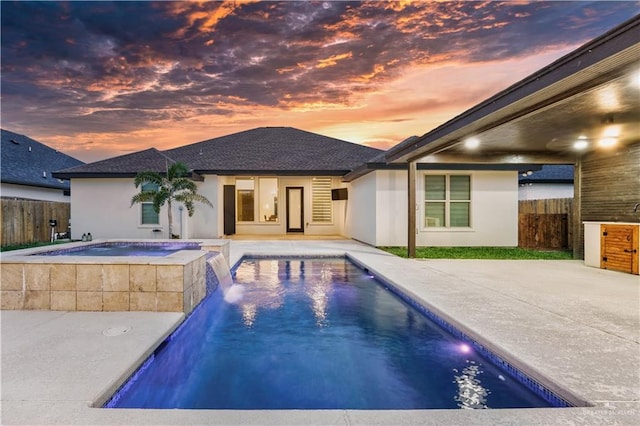 pool at dusk featuring an in ground hot tub, pool water feature, and a patio