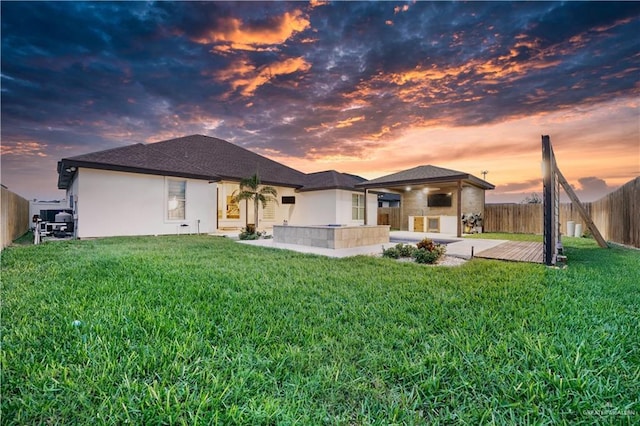 back house at dusk with a lawn and a patio area