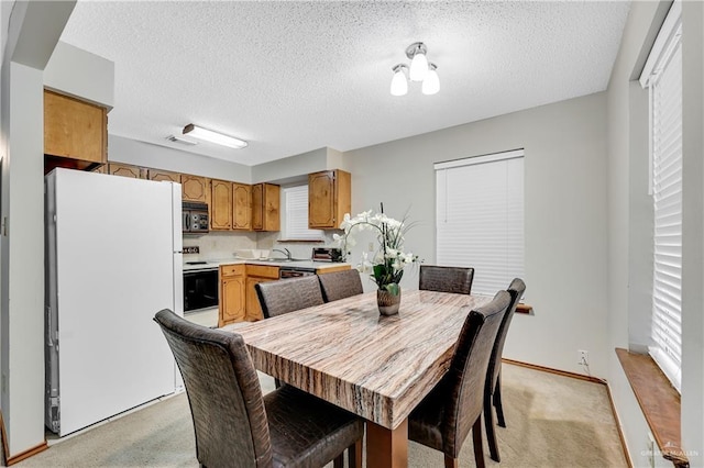 dining area with light colored carpet, sink, and a textured ceiling