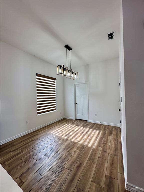 2413 N Woody St, Edinburg, TX 78541 - unfurnished dining area with wood finished floors, baseboards, and a chandelier