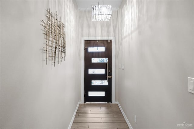 doorway to outside featuring a chandelier, wood finish floors, and baseboards