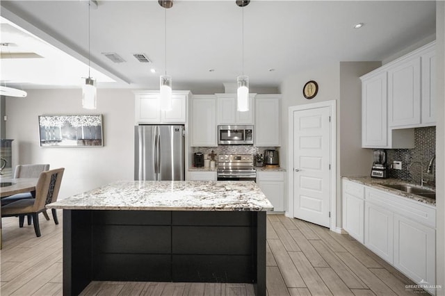 kitchen featuring white cabinets, a kitchen island, hanging light fixtures, stainless steel appliances, and a sink