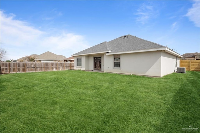 rear view of house featuring a yard, stucco siding, a shingled roof, central AC, and a fenced backyard