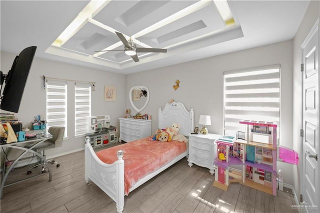 bedroom featuring a ceiling fan, a tray ceiling, multiple windows, and wood finished floors