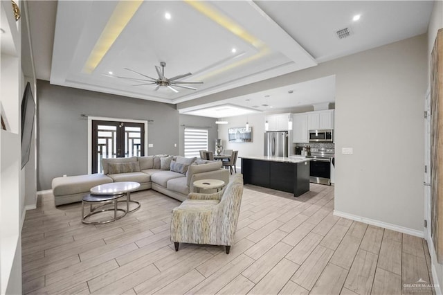 living area with a ceiling fan, baseboards, visible vents, wood tiled floor, and a tray ceiling