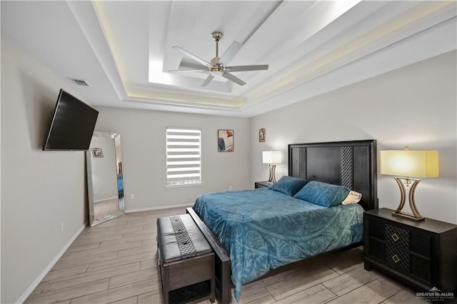 bedroom featuring baseboards, a tray ceiling, visible vents, and wood tiled floor