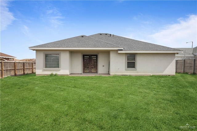 back of house with a fenced backyard, a shingled roof, a lawn, and stucco siding