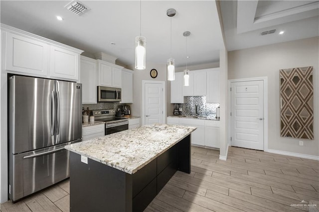 kitchen featuring white cabinets, stainless steel appliances, decorative light fixtures, and a center island